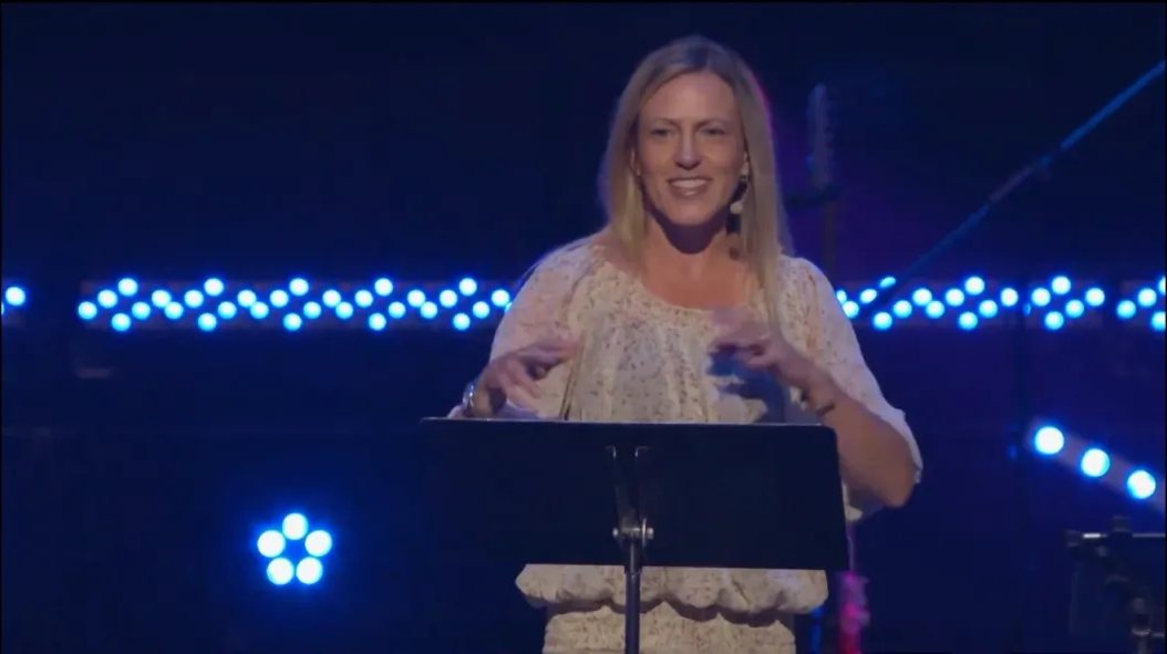 Valerie speaking on a stage lit with blue lights
